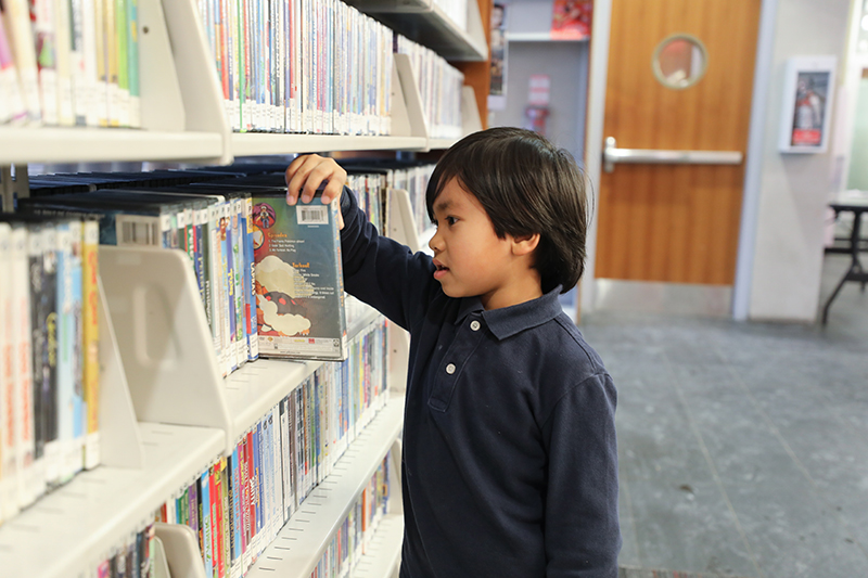 Child browses children’s books on shelf in a library.