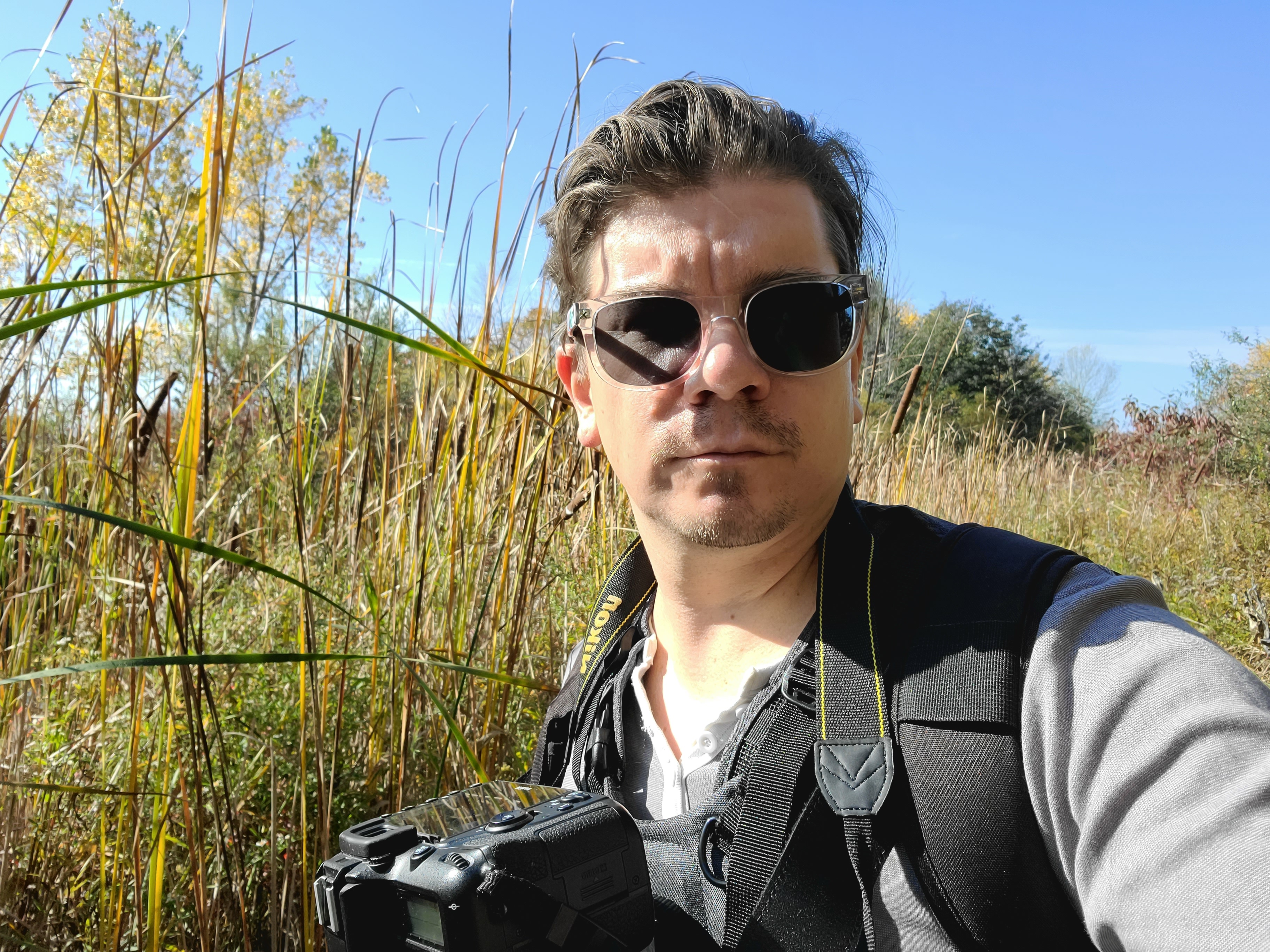 Nathan Cole in a field holding a camera.