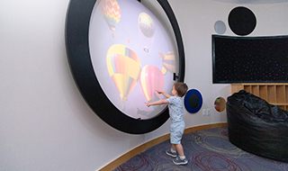 A young customer plays around with the image projector. It’s an easy-to-use, lightweight projector with three rotating image wheels that are projected onto framed circle on the Sensory Room wall.