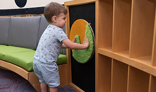A young customer twists one of the wall mounted tactile circles that provides visual and tactile sensory input for kids to explore through various colours and textures.