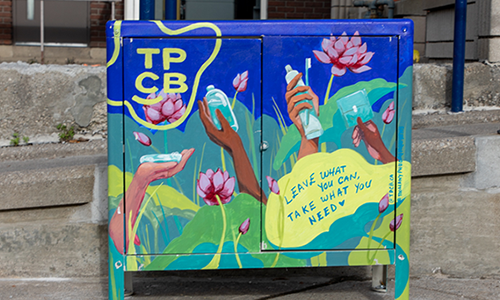 Cabinet outside the branch with painted art of hands holding different personal care products and text that reads: “leave what you can take what you need” and “TPCB.”.