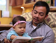 Child sitting on father's lap while reading a book