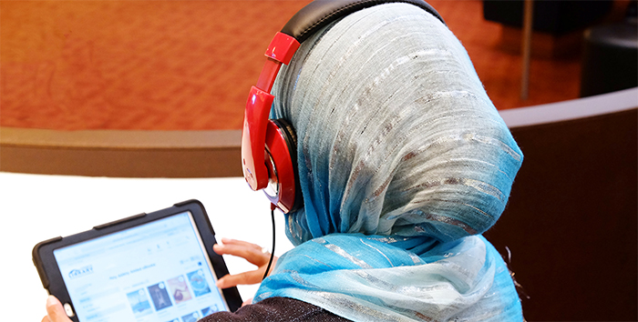 A woman wearing a light blue headscarf and red headphones is browsing for audiobooks on a tablet.