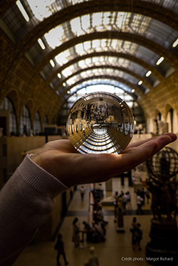 Image créée par Margot Richard : une main tenant une boule de cristal avec le reflet du hall principal du Musée d'Orsay en arrière-plan.